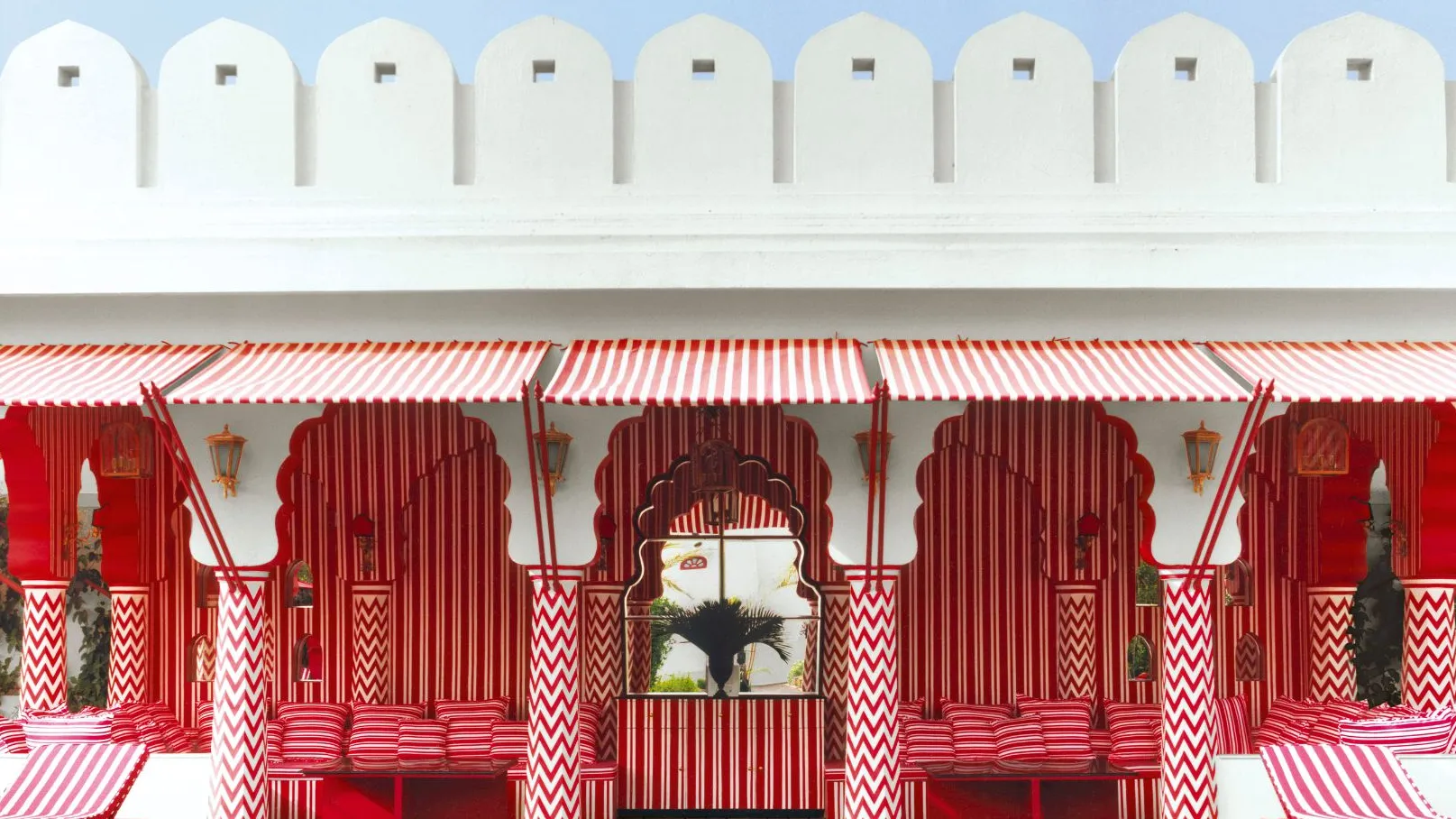 A colorful outdoor space at Villa Palladio in Jaipur, featuring a white wall with a red striped awning, red and white striped columns, and a glimpse of a red and white striped interior